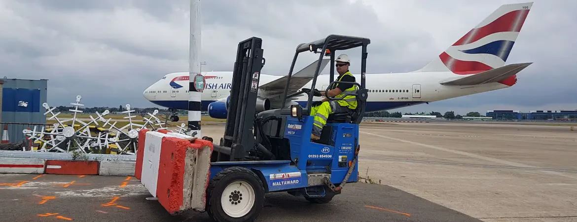 A forklift with driver on the apron at a international airport with a large jumbo jet in the background.