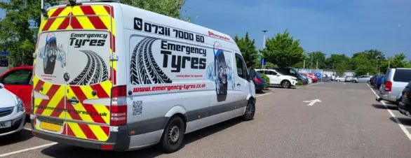 A business transit van with company details on the side and back driving through a car park.